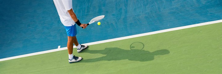 Man bouncing tennis ball from racket on green and blue court